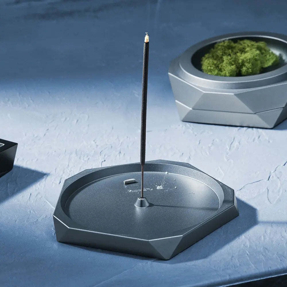 Hexagonal incense burner with a single incense stick on a textured blue surface.