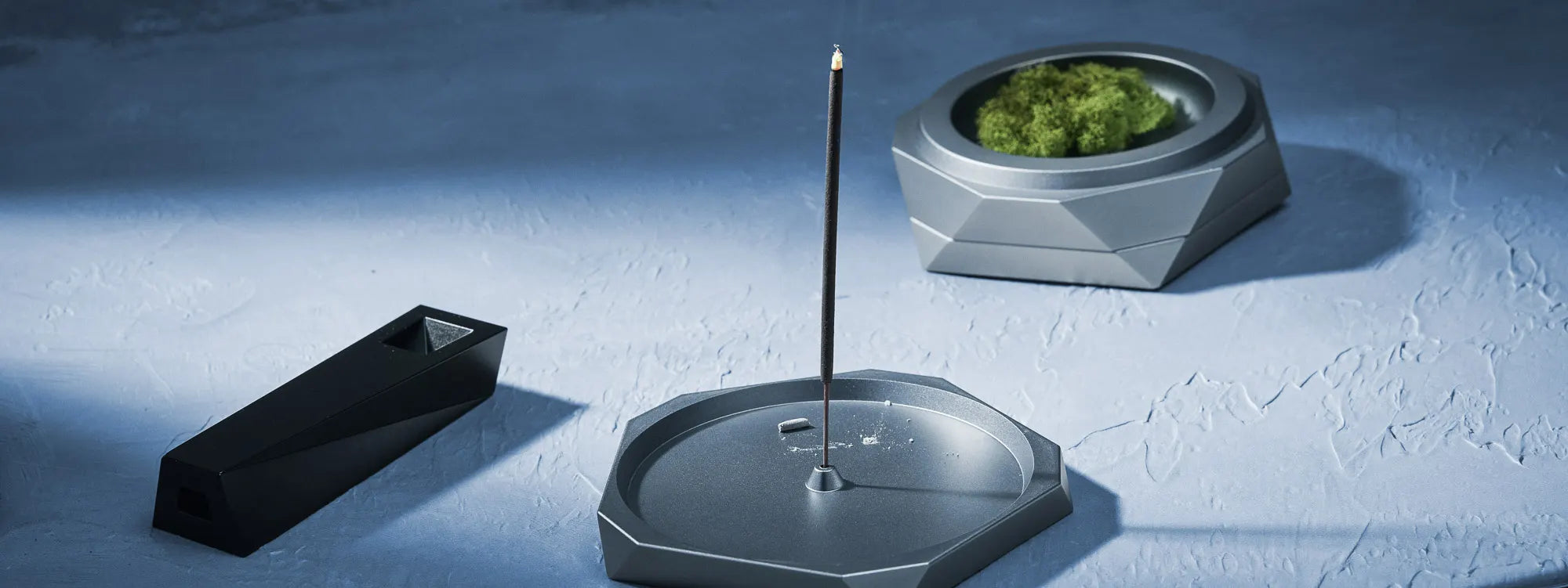 Incense burner with incense stick and green incense on a textured blue surface