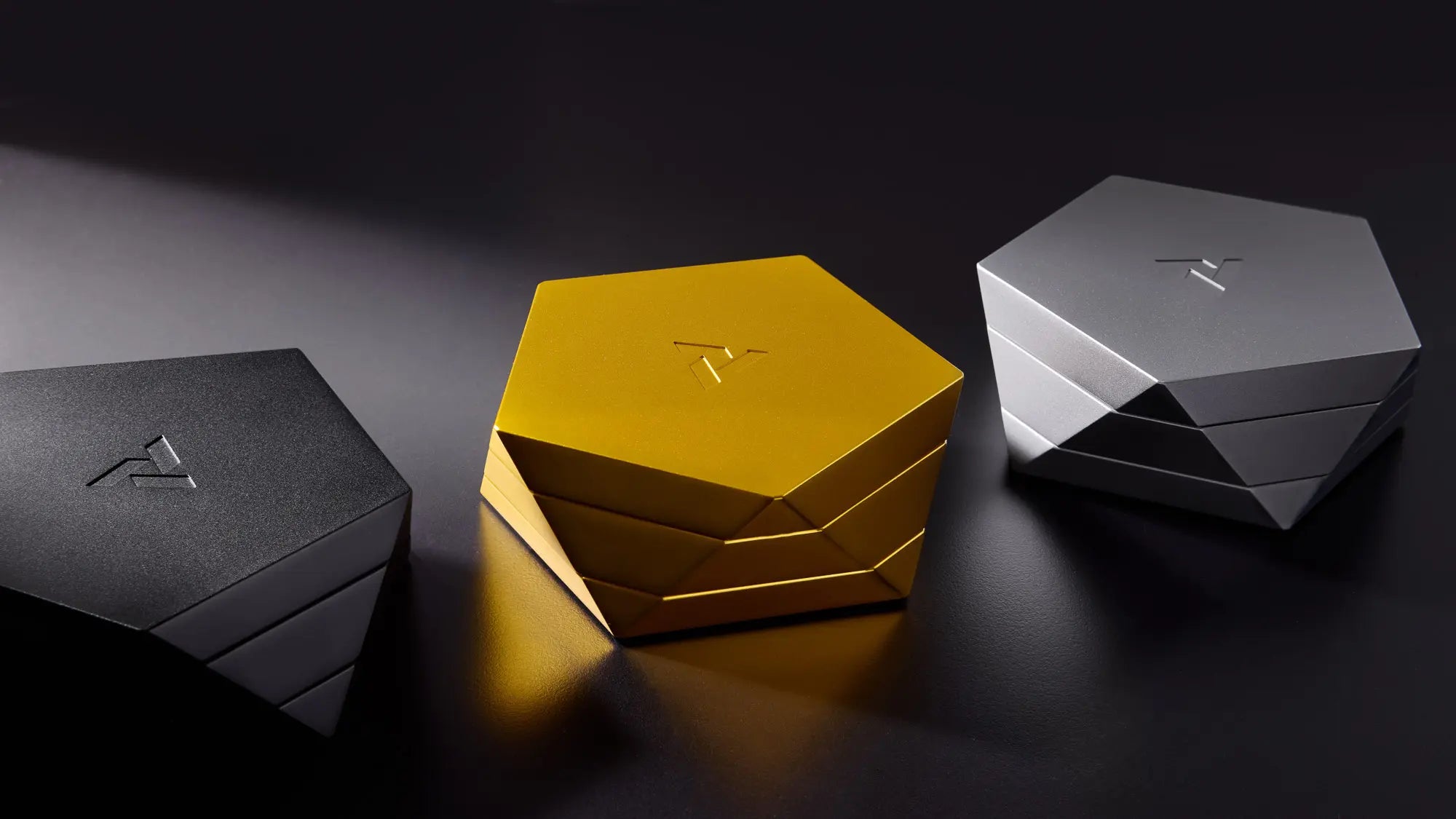 Three geometrically shaped boxes in black, gold, and silver on a dark background